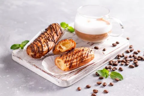 Chocolate Cream Filled Eclair on a white wooden board on a light stone backgr Stock Photos