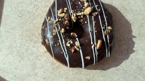A chocolate donut sprinkled with nuts rotates in a circle on a white surface Stock Footage 307429214