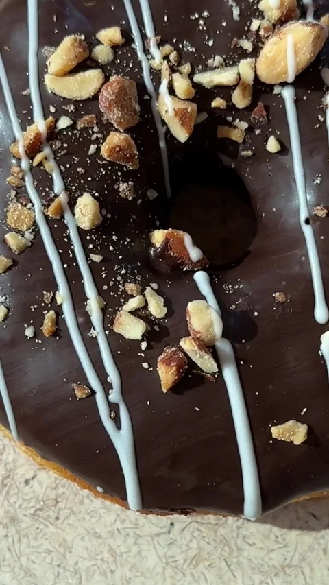 A chocolate donut sprinkled with nuts rotates in a circle on a white surface Stock Footage 307861349