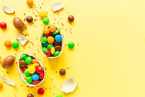 Chocolate Easter eggs and colorful candies on yellow paper background. flat l 스톡 사진