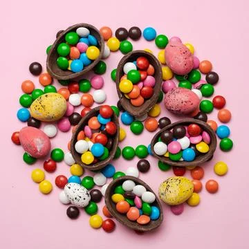 Chocolate easter eggs and sweet candies on pink background with copy space... Stock Photos
