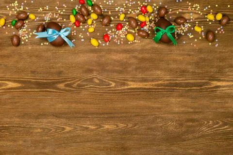 Chocolate Easter eggs and sweets over brown wooden background. Empty space fo Stock Photos