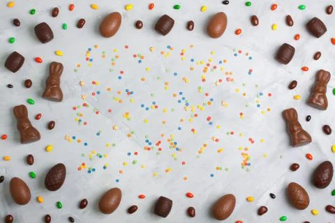 Chocolate easter eggs, rabbits, casks, sweets, confetti on concrete backgroun Stock Photos