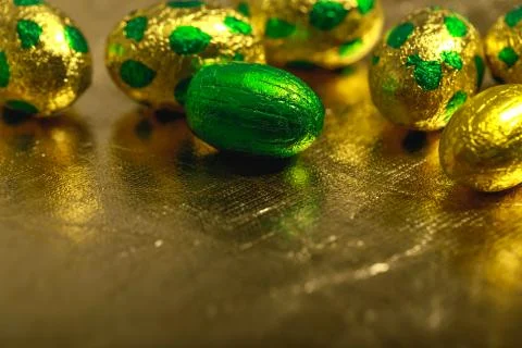 Chocolate easter eggs wrapped in yellow gold and green colored foil on golden Stock Photos