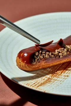 Chocolate eclair with brown glaze in a plate on a brown background. Stock Photos