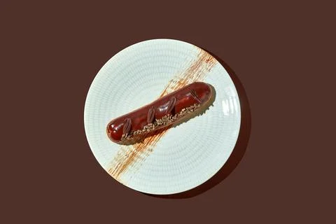 Chocolate eclair with brown glaze in a plate on a brown background. Stock Photos