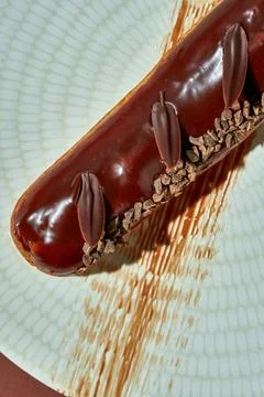 Chocolate eclair with brown glaze in a plate on a brown background. Stock Photos