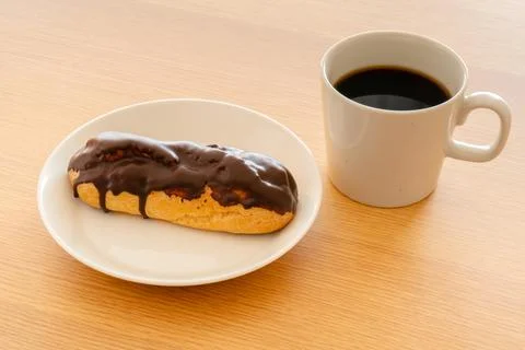 A chocolate eclair on a white dish and a cup of coffee Stock Photos