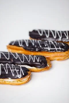Chocolate eclairs sit on a white surface ready to be enjoyed 库存照片