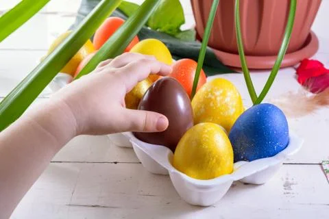Chocolate egg among colored easter eggs. Child's finger pointing at a choco.. Stock Photos