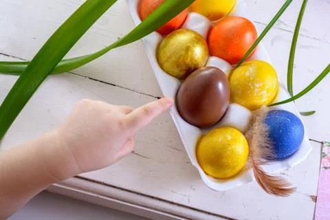 Chocolate egg among colored easter eggs. Child's finger pointing at a choco.. Stock Photos