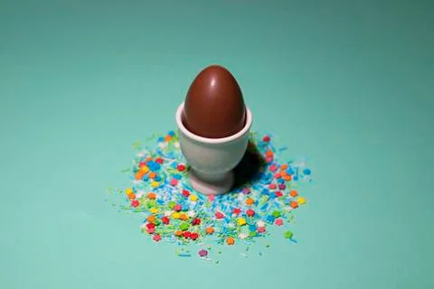 A chocolate egg in a white egg stand with sweet powder on a green background Stock Photos