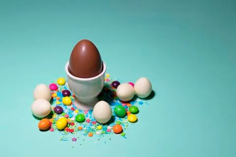 A chocolate egg in a white egg stand surrounded by sweets on a green background Stock Photos