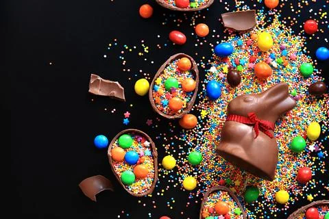 Chocolate eggs and rabbit, sugar colored sprinkles on a black background Stock Photos