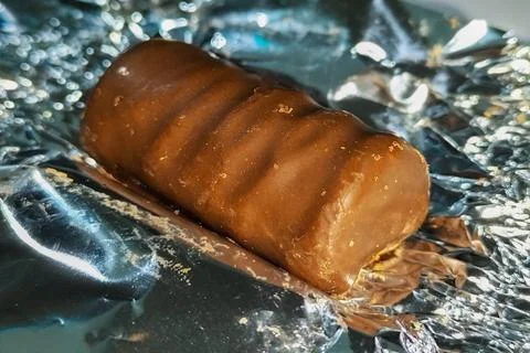Chocolate-glazed candy on an open silver wrapper close-up. Confectionery an.. Stock Photos