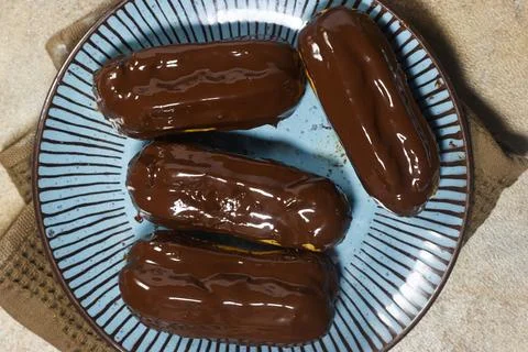 Chocolate Glazed Éclair On Plate With More Pastries In Soft Focus Background Stock Photos
