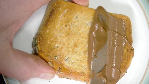 Chocolate hazelnut spread being added onto a piece of toast. Video stock 264107074
