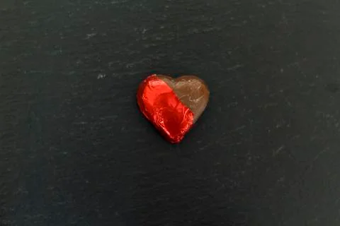 Chocolate Heart with wrapping half open on black background Stock Photos