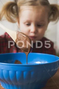 Chocolate Icing Running From Wooden Spoon, Child In Background