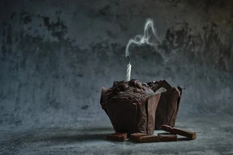 Chocolate muffins on a dark background with an extinguished candle Stock Photos