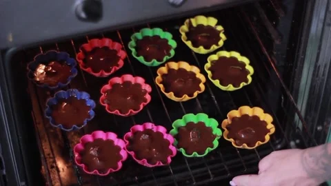 Chocolate muffins in multi-colored forms are laid in the oven Stock Footage 198526683