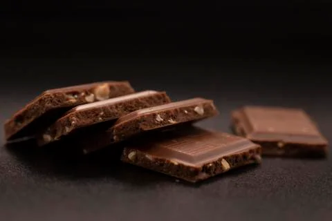 Chocolate with nuts. Chunks of chocolate with nuts on a dark background. Stock Photos