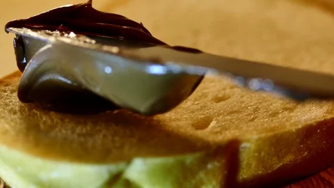 Chocolate paste with a knife is smeared on a piece of white bread. To prepare a Stock Footage 84832696