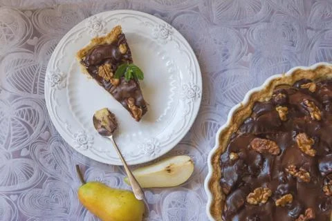 Chocolate pear pie. Portion slice on a white plate and a quarter tart on a Stock Photos