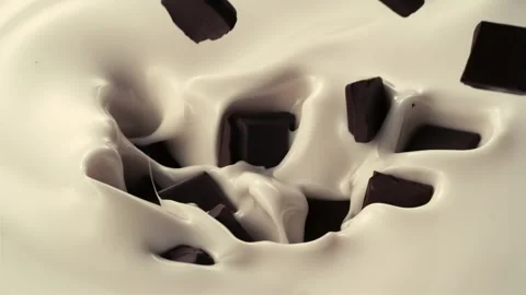 Chocolate pieces fall down into pouring creamy milk in slow motion Stock Footage 147509942