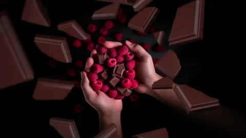 Chocolate pieces spiraling and falling into human hands holding raspberries Stock Footage 258501728