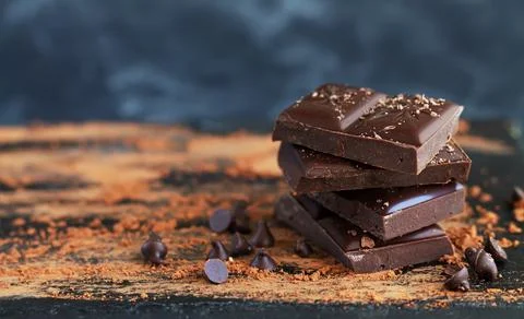 Chocolate pieces stack with chocolate flakes, drops and cocoa powder on dark Stock Photos