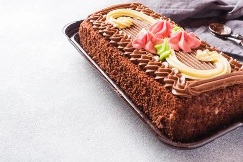 Chocolate rectangular cake decorated with cream roses on a light table. Swe.. Foto stock