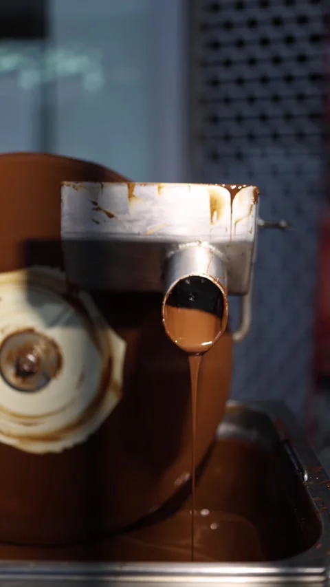 A chocolate refining machine dispensing a smooth stream of melted chocolate. The Stock Footage 289634685