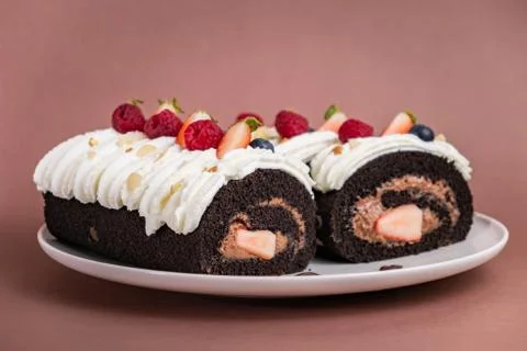 Chocolate roll cake with berries and fresh cream on brown background. Stock-Fotos