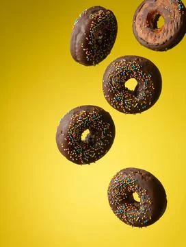 Chocolate round donuts with multicolored sugar sprinkles levitate on a yell.. Stock Photos