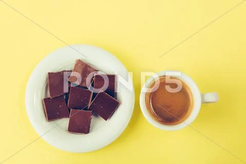Chocolate on a saucer and a cup of coffee on a yellow surface Stock Photos