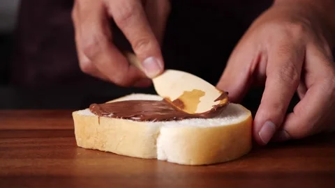 Chocolate Spread for breakfast. Men hand spreading hazelnut cream on slice bread Stock Footage 142486014