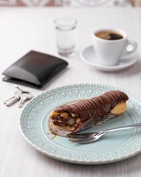 Chocolate stuffed eclair on a green plate with coffee and personal objects .. Stock Photos