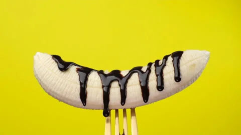 Chocolate syrup flows down on banana close up on yellow background Stock Footage 145342054