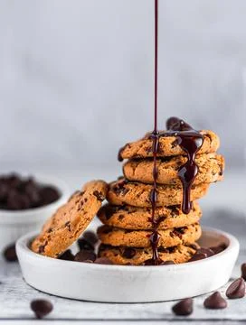 Chocolate syrup pouring on a stack of chocolate chip cookies on white plate Stock Photos