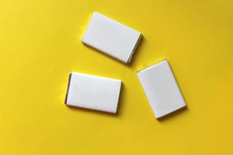 Chocolates wrapped in silver foil and white blank paper isolated on yellow su Stock Photos