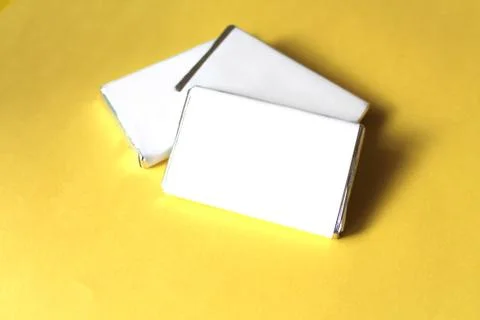Chocolates wrapped in silver foil and white blank paper isolated on yellow su Stock Photos