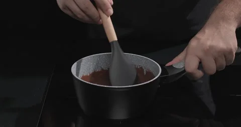 Chocolatier melts dark chocolate in a pan over black background. Cooking Stock Footage 250225962