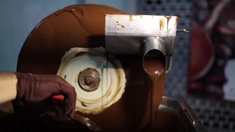 A chocolatier operates a refining machine, guiding a steady flow of melted choco Stock Footage 289634540