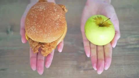 Choose between a calorie burger and a green apple. Women's hands hold harmful Stock Footage 132203186