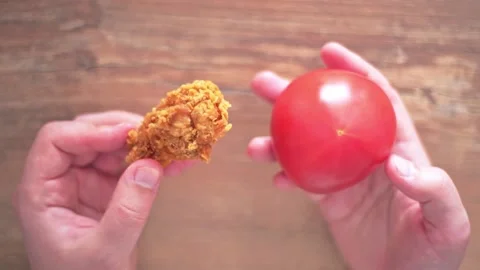 Choosing between healthy and harmful food. Fried chicken and fresh tomato in Video stock 131991872