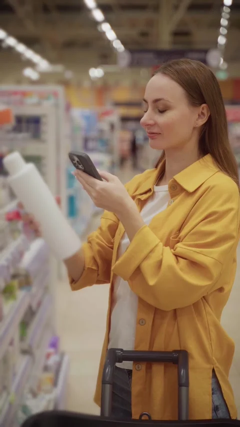 Choosing the right shampoo at a local store while checking product details on a 스톡 동영상 305415230