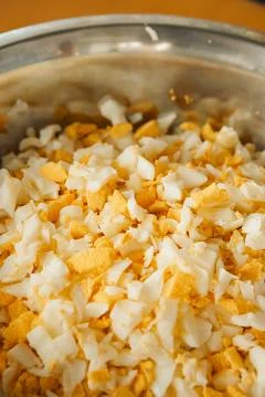 Chopped boiled eggs mixed with cheese in a metal bowl on a wooden table durin Stock Photos