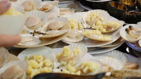 Chopped cheese is being sprinkled over many scallops, adding a rich, savory Stock Footage 311749346