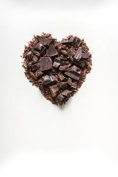 Chopped dark chocolate folded in the shape of a heart on a white background.  Stock Photos